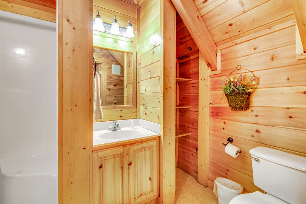 A bathroom with wooden walls, a white sink, toilet, and shower