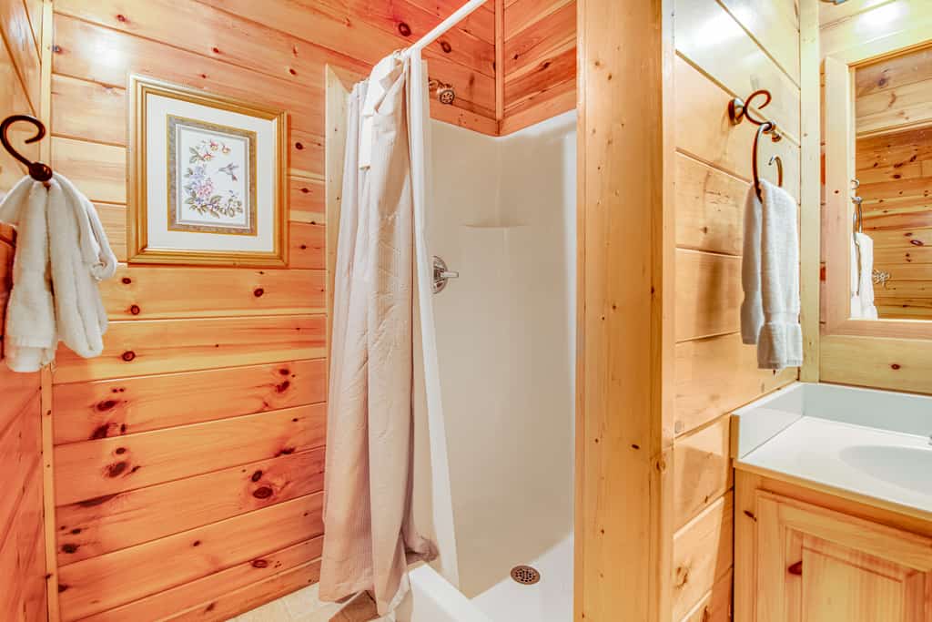A bathroom with a shower, sink, and mirror, featuring wood paneling and towels.