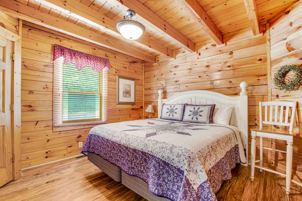 A wide-angle view of a cozy room with a queen-sized bed, wooden paneling, and a vaulted ceiling.