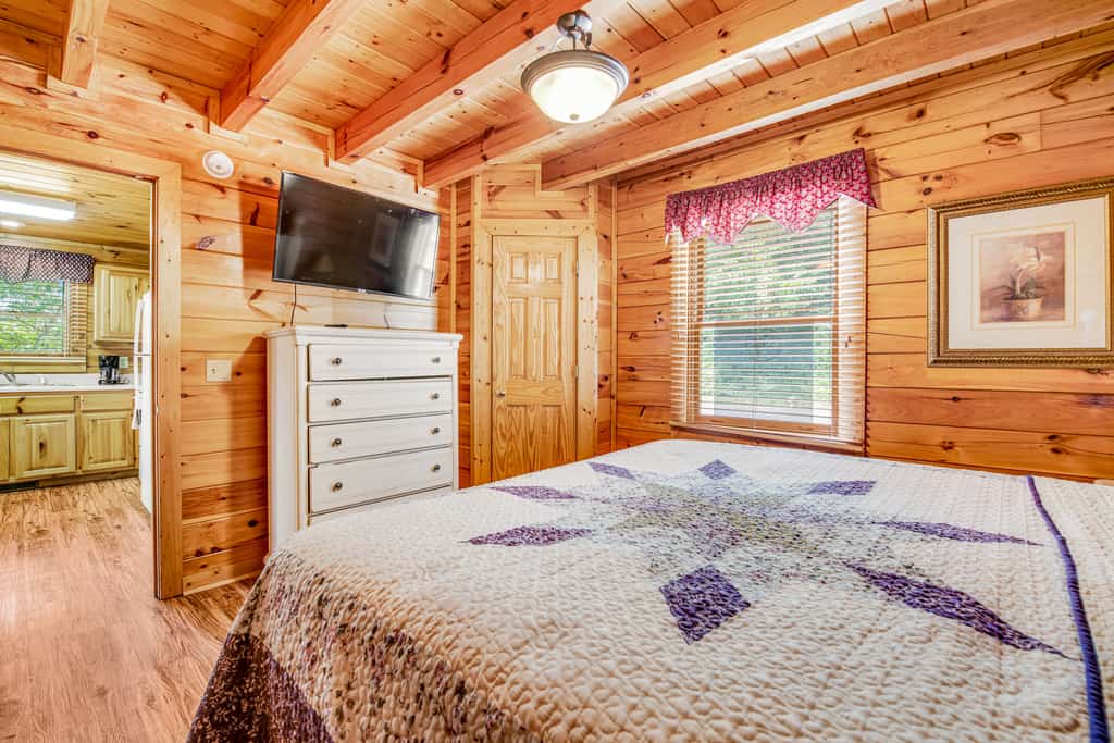 A log cabin room with a bed, TV, and dresser
