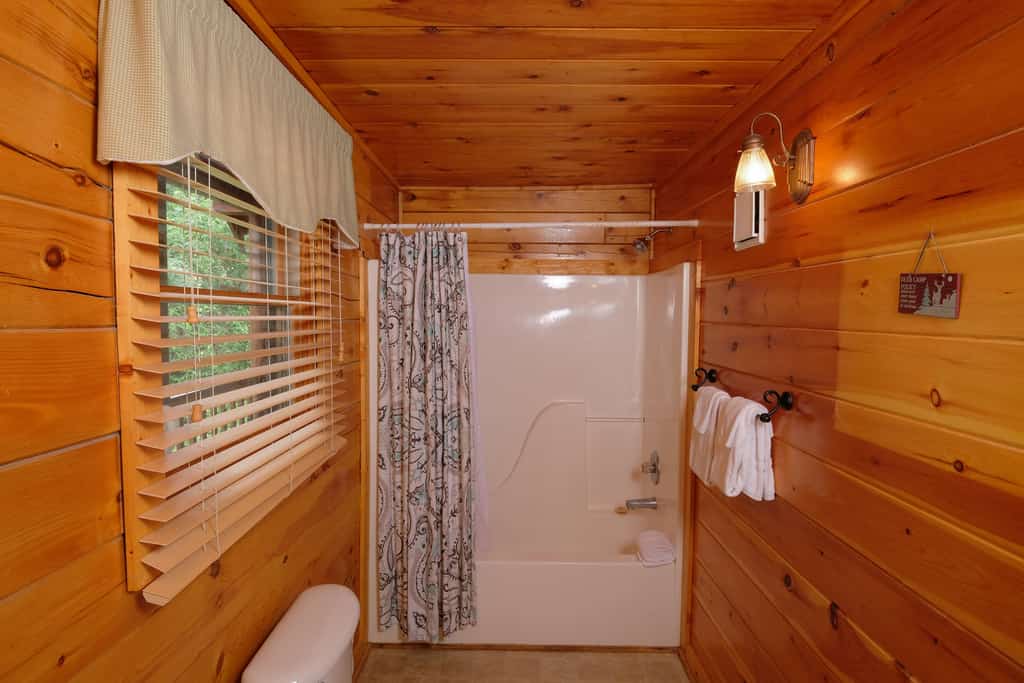 A bathroom with a tub and shower, log cabin style wood paneling, and a window