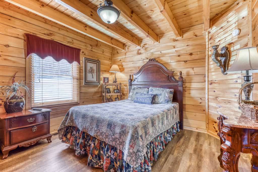 A cozy log cabin-style room with a large bed, wooden furniture, and exposed beams.