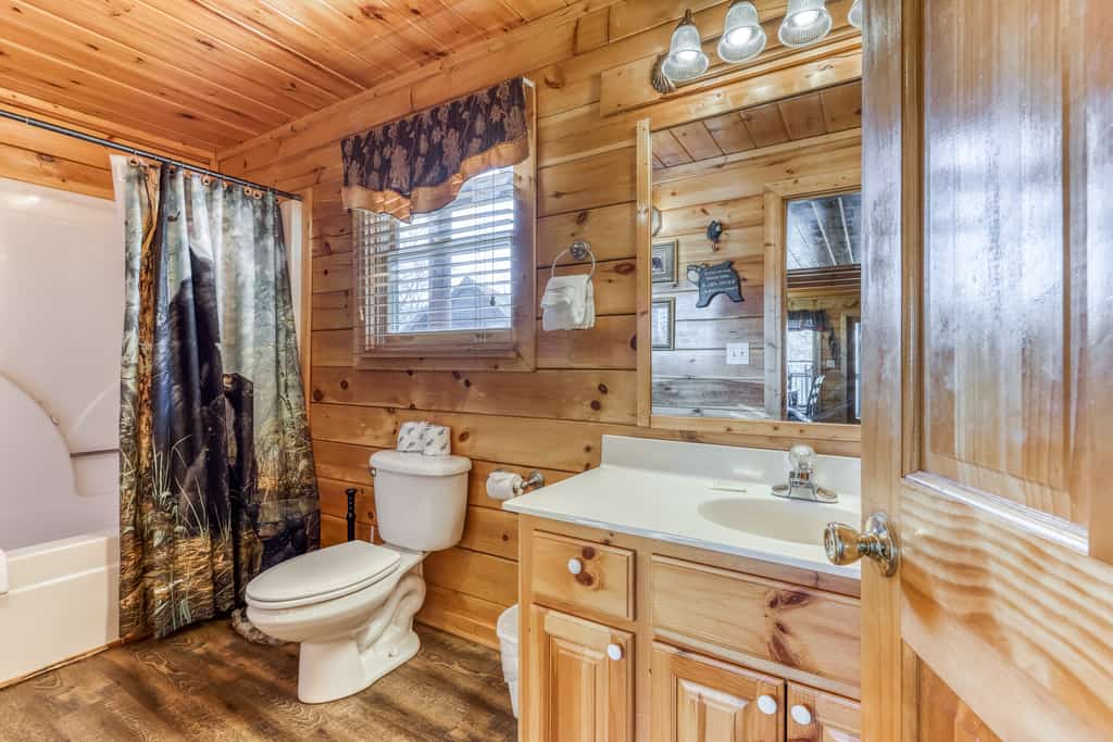 A bathroom with wood paneling, a toilet, sink, and shower.