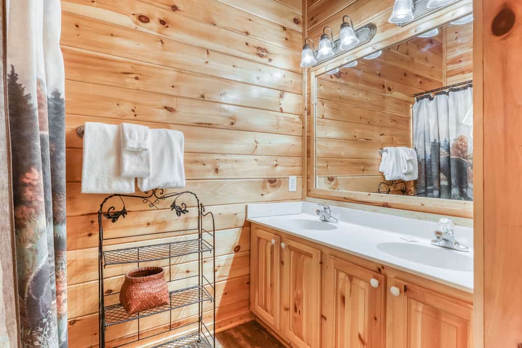 A bathroom with light wood paneling, a double vanity with a large mirror, and towels on a shelf.
