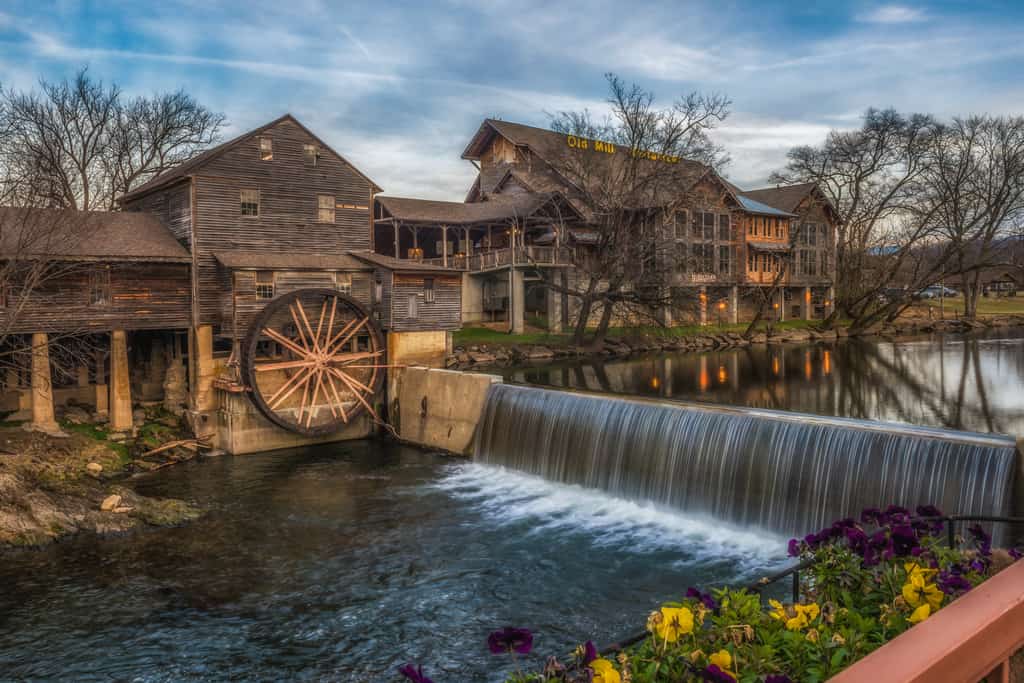 A wide exterior view of a large building with a water wheel and a waterfall in front of it.