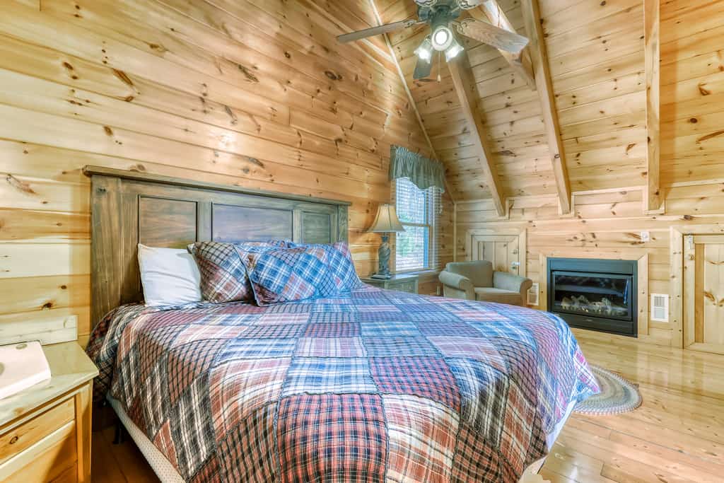A cozy room with a large bed, wooden paneling, and a fireplace.