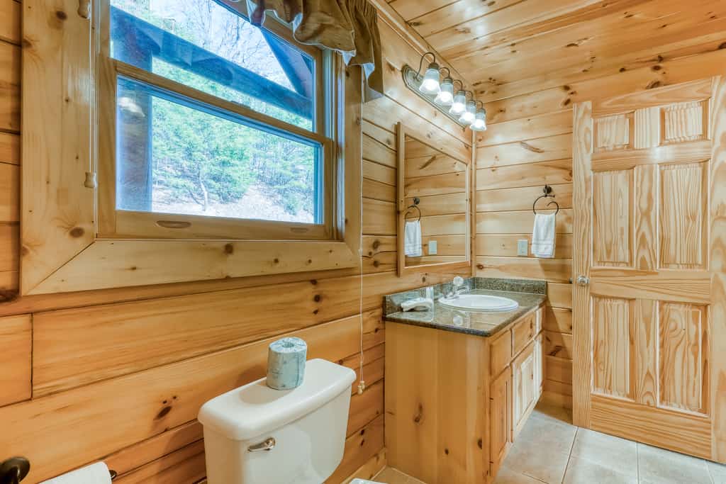 A bathroom with wooden walls, a toilet, a sink, and a window.