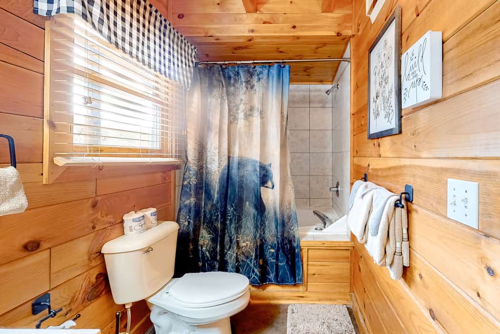 A bathroom with a toilet, shower, and bathtub, featuring wooden walls and a blue shower curtain.