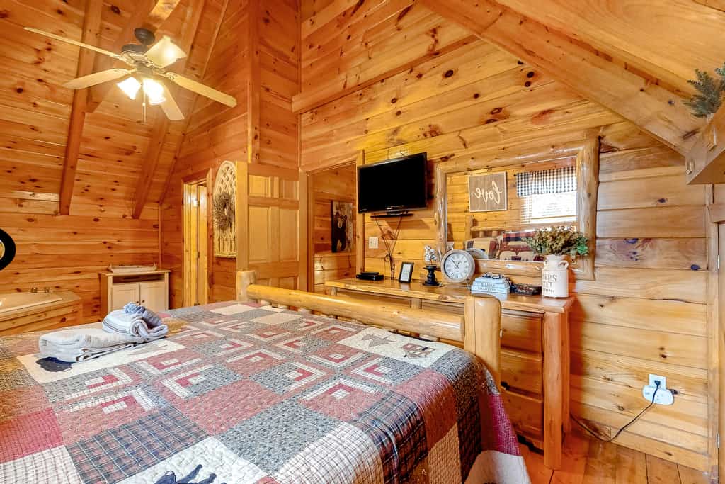 A wide-angle view of a cozy room with wood paneling, a vaulted ceiling, and a large bed.