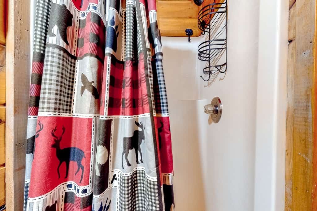 A shower area with a red, black, and white plaid shower curtain featuring wildlife designs, wooden accents, and a white bathtub.