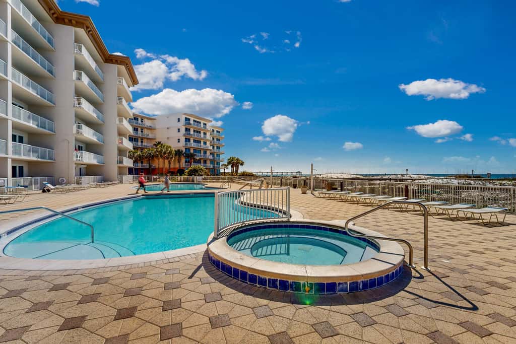 Beachfront condo with beach chairs, an umbrella, and a pool