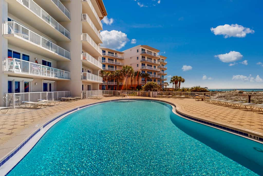 Beachfront condo with beach chairs, an umbrella, and a pool