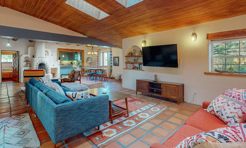 Welcome to Bedside Manor, a character-filled adobe home on a lush .76-acre lot just minutes from Downtown Taos. Soak in the private hot tub under the stars, gather around the kiva fireplace beneath soaring viga-and-skylight ceilings, and grill dinner by the covered outdoor fireplace. With two king bedrooms, a futon study, a spa-like bath, mountain views, and room for the whole family plus a dog, this single-level retreat is a peaceful Taos basecamp.