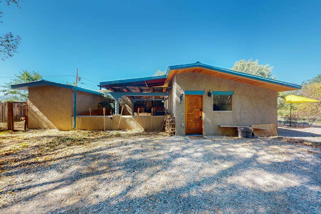 Welcome to Bedside Manor, a character-filled adobe home on a lush .76-acre lot just minutes from Downtown Taos. Soak in the private hot tub under the stars, gather around the kiva fireplace beneath soaring viga-and-skylight ceilings, and grill dinner by the covered outdoor fireplace. With two king bedrooms, a futon study, a spa-like bath, mountain views, and room for the whole family plus a dog, this single-level retreat is a peaceful Taos basecamp.