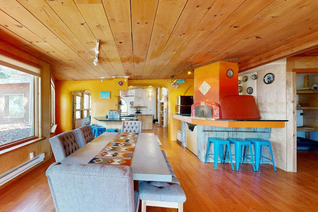 Tucked behind a private gate on a pinon-dotted mesa between Taos and Taos Ski Valley, this one-of-a-kind adobe hideaway is built for slow mornings and long mountain views. Cook in a kitchen built around a showpiece pizza oven, gather by the kiva fireplace, and unwind in the spa-like primary suite. Two living areas, three bedrooms, and walls of glass framing the Sangre de Cristos make easy room for nine - and the dogs are welcome too. Peace, pizza, and big New Mexico sky await.