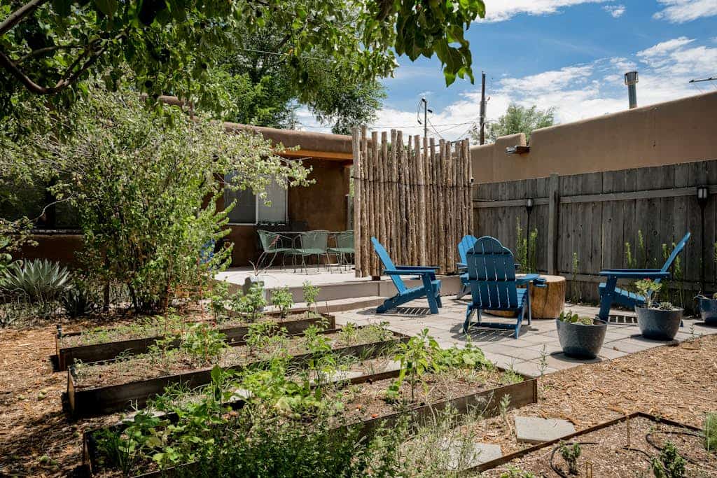 Welcome to Santa Fe Serenity, a light-filled home tucked behind private adobe walls just a short walk from the Railyard District. Step inside to warm terracotta tile, skylights, and a cozy living room anchored by a wood stove, then gather around the dining table or cook in the fully equipped kitchen. Two queen bedrooms with ceiling fans and hardwood floors make it easy to settle in, while the walled backyard, with its covered deck, fire feature, and flourishing garden of raised beds and fruit trees, invites slow mornings and golden-hour evenings. Minutes from the Plaza, world-class museums, and Santa Fe's celebrated food scene, this dog-friendly, 1,005 sq ft retreat is the perfect base for exploring the City Different.