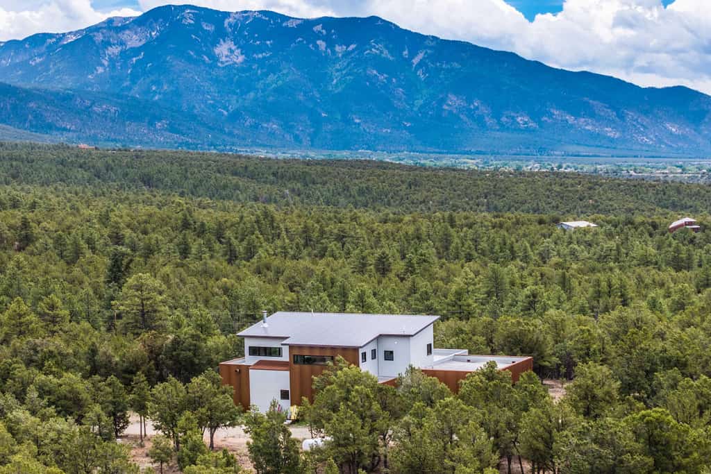 Welcome to Piñon Ridge Retreat, a striking modern home tucked into the piñon forest above Valdez, where walls of glass frame the Sangre de Cristo peaks from nearly every room. Wake to forest light in ground-floor bedrooms, gather in the window-wrapped upper living space, and step onto the deck to grill at sunset. Soak in the private hot tub under the stars, trade volleys at the ping pong table, and unwind by the fire. Modern, secluded, and quiet, with Taos and the Ski Valley a short drive away.