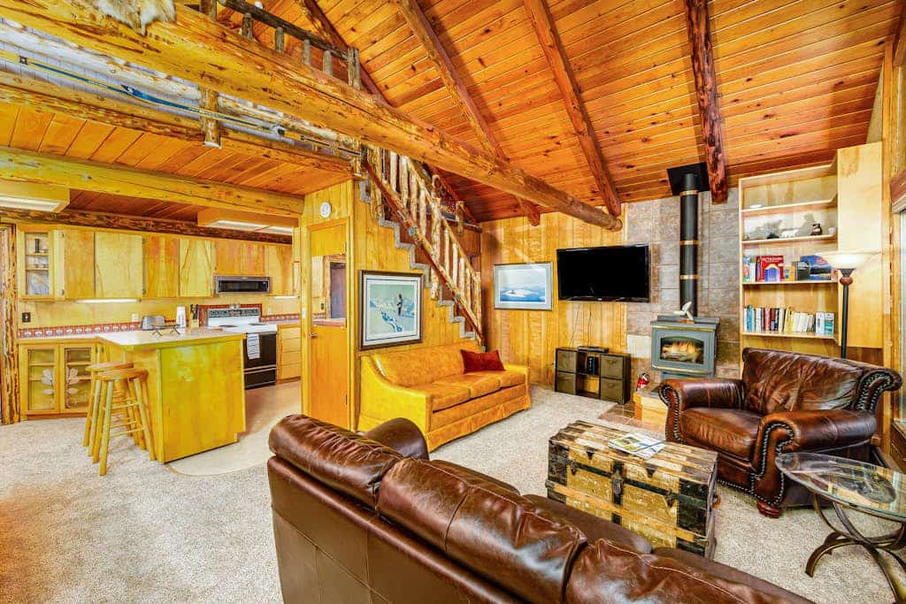 Log cabin living executed exactly the way it should be. Alpine Meadows Log Cabin sits a mile from Girdwood Park and minutes from the direct base of Alyeska Resort—offering a clean mountain escape that allows you to completely disconnect from the digital noise. The architecture features massive traditional log walls, a forest closing in on all sides, an expansive wrap-around deck built for summer sunbathing or stargazing, and large picture windows that flood the rustic space with natural light. Stowe the central wood stove on cold winter nights, cook real meals in the full kitchen, and use the private washer and dryer to keep gear dry. Standard Specs: Fully equipped kitchen with complete cookware, traditional wood stove, expansive private deck, private in-unit washer/dryer, flat-screen TV, high-speed WiFi, and keypad entry. Driveway parking for two vehicles. Sleeps 6.