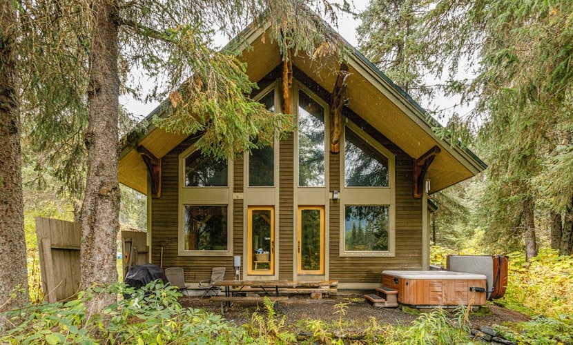 There is a moment when the highway falls away, the spruce closes in, and the only sound is the water out back. That is Iris Pond. Handcrafted with custom wood-carved interiors, this private Girdwood cabin pairs rugged Alaska character with polished hospitality, sitting just a few minutes from the chairlifts at Alyeska. The open layout features large windows framing the forest, a fully equipped chef's kitchen, and a seamless transition to the back deck where a private hot tub waits beneath the trees. It is a quiet, clean basecamp built for slow mornings with local coffee and long evenings after hiking Chugach National Forest trailheads or chasing deep powder. Standard Specs: Fully equipped kitchen, private washer/dryer, flat-screen TV, high-speed WiFi, and keypad entry. Safe parking for up to four vehicles. Sleeps 7.
