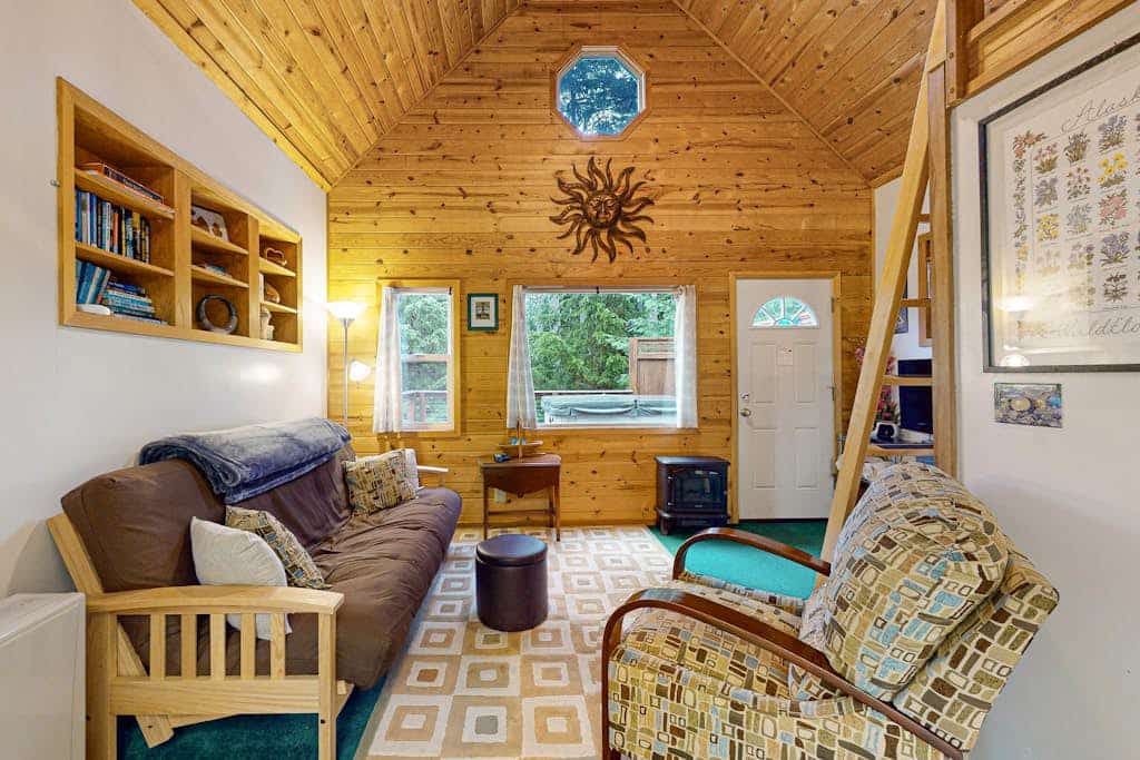 Christina Cabin is small on purpose. Tucked quietly into the forest under two miles from Alyeska Resort, this quaint alpine A-frame is an intentional, artsy retreat where the noise of the rest of the world completely disappears. The hand-styled interior features custom personal touches and high-quality furnishings, while the back patio holds a brand-new private hot tub enclosed by a custom wood privacy fence. Walk straight out your door to access local hiking loops, or take a quick drive to the village dining spots and aerial tramway. A clean, romantic space built for purists. Standard Specs: Well-equipped kitchen, private outdoor hot tub with privacy fencing, flat-screen TV, high-speed WiFi, and keypad entry. Driveway parking for two vehicles. Strict compliance with local quiet hours (10 PM–8 AM) and non-smoking premises. Sleeps 2.