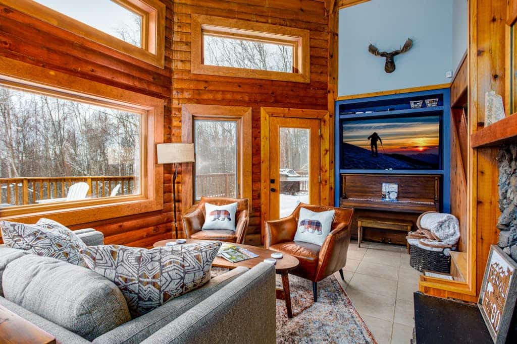 Twenty minutes north of downtown Anchorage, the city quiets and the birch forest takes over. Queens Birch Lodge is a cabin-styled retreat tucked deeply into that canopy—featuring towering windows that bring the old-growth woods into nearly every room. The outdoor living area is built for long northern evenings, offering a porch swing out front, an upscale hot tub on the back deck, a private gas grill, and a premium fire table. Inside, discovery awaits with a gas fireplace, a full kitchen with a granite prep island, an upright piano, and a dedicated executive home office space. Standard Specs: Full kitchen with granite island, private hot tub, fire table, gas fireplace, upright piano, standalone office desk, private laundry, high-speed WiFi, and keypad entry. Driveway parking for up to three vehicles. Enforces strict maximum occupancy rules. Sleeps 6.