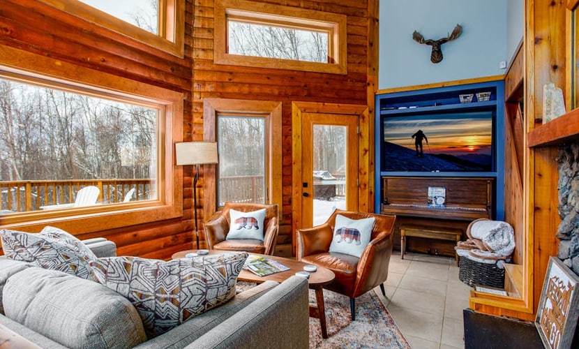 Twenty minutes north of downtown Anchorage, the city quiets and the birch forest takes over. Queens Birch Lodge is a cabin-styled retreat tucked deeply into that canopy—featuring towering windows that bring the old-growth woods into nearly every room. The outdoor living area is built for long northern evenings, offering a porch swing out front, an upscale hot tub on the back deck, a private gas grill, and a premium fire table. Inside, discovery awaits with a gas fireplace, a full kitchen with a granite prep island, an upright piano, and a dedicated executive home office space. Standard Specs: Full kitchen with granite island, private hot tub, fire table, gas fireplace, upright piano, standalone office desk, private laundry, high-speed WiFi, and keypad entry. Driveway parking for up to three vehicles. Enforces strict maximum occupancy rules. Sleeps 6.