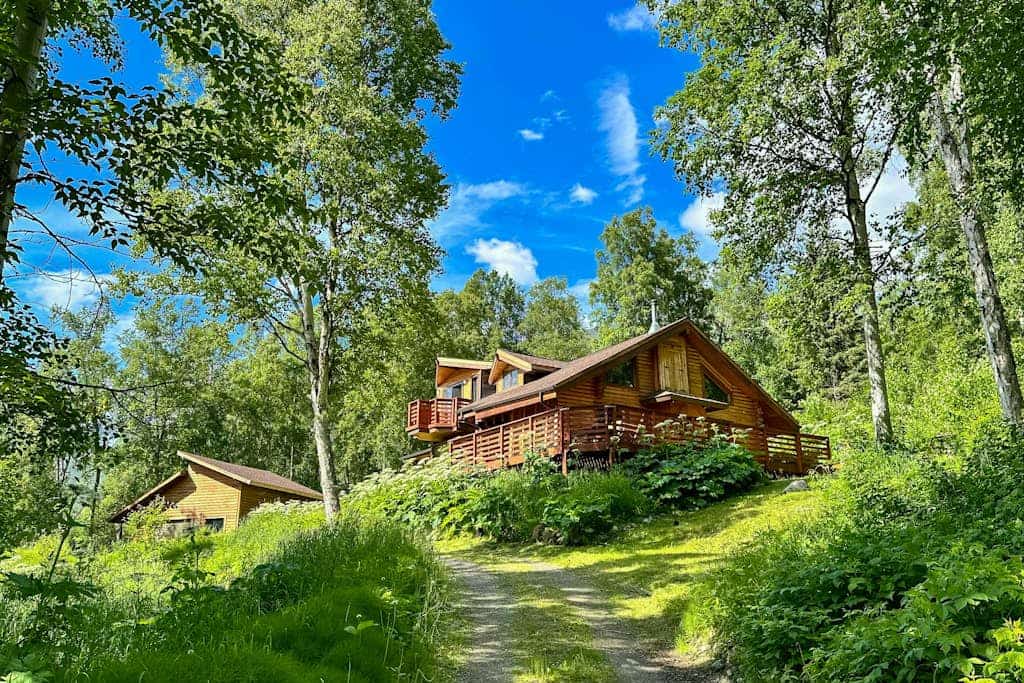 The cabin sits exactly where the road runs out—thirty minutes outside of Anchorage and fifteen minutes from downtown Eagle River, completely embedded inside a rugged wilderness where moose move through the yard and the northern lights handle the winter sky. Constructed with traditional log walls and framing picture windows, the home features a classic wood stove, a master bedroom loft with an en-suite bath, and a large viewing deck. Engineered for remote professionals, the cabin includes dedicated high-speed WiFi and a workspace docking station packed with two desktop monitors. Located two miles from the Eagle River Nature Center trail loops and salmon-viewing deck. *Winter notice: 4WD strictly required.* Standard Specs: Fully equipped kitchen with dishwasher, wood stove, executive desk workspace with dual monitors, viewing deck, private laundry, high-speed WiFi, and safety tools. Driveway parking for three vehicles (steep loop). Dog-friendly. No parties/strict quiet hours. Sleeps 6.