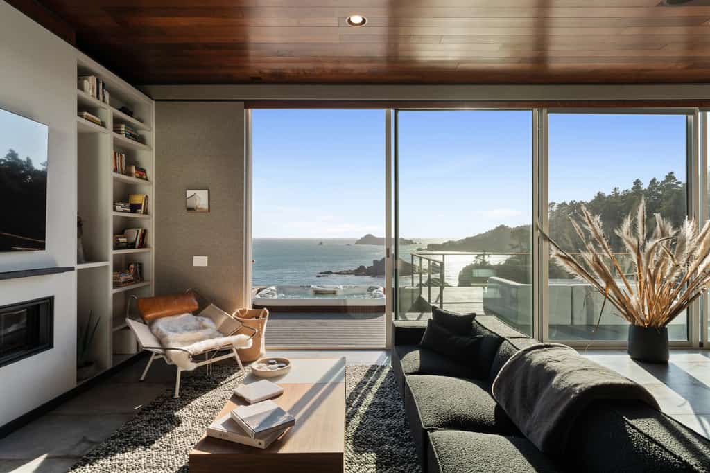 Floor-to-ceiling glass, a private cove, and the Pacific straight ahead. The house is concrete, steel, and wood on 5.25 acres of bluff at Anchor Bay, with 1,800 feet of oceanfront below it and rock islands offshore where the seals bark and, in winter, whales pass close enough to watch from the hot tub. Three suites sleep 8 — two kings and a bunk room. Evenings go to the deck: the 6-person hot tub, the fire pit, the bench at the edge of the bluff, and whatever the sunset decides to do.