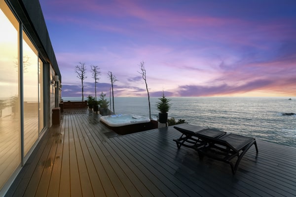 Floor-to-ceiling glass, a private cove, and the Pacific straight ahead. The house is concrete, steel, and wood on 5.25 acres of bluff at Anchor Bay, with 1,800 feet of oceanfront below it and rock islands offshore where the seals bark and, in winter, whales pass close enough to watch from the hot tub. Three suites sleep 8 — two kings and a bunk room. Evenings go to the deck: the 6-person hot tub, the fire pit, the bench at the edge of the bluff, and whatever the sunset decides to do.