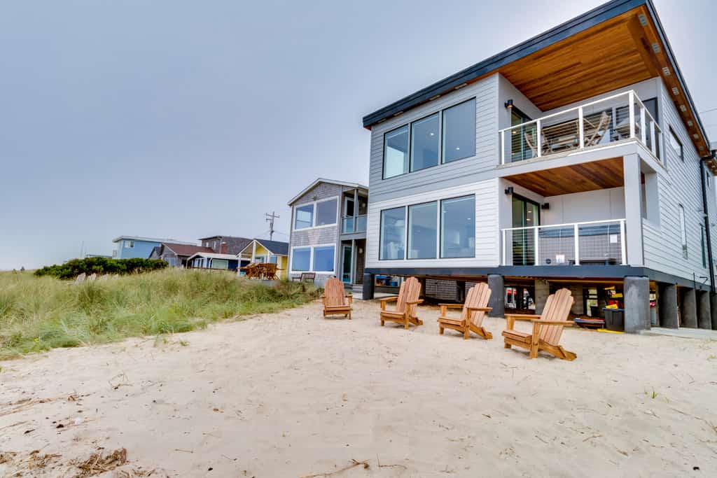 four adirondack chairs sit in the sand outside of this modern rockaway beach vacation rental