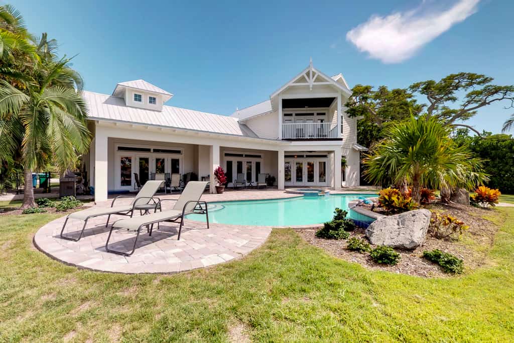 Large vacation home with an outdoor pool and a yard with palm trees in Holmes Beach, FL.