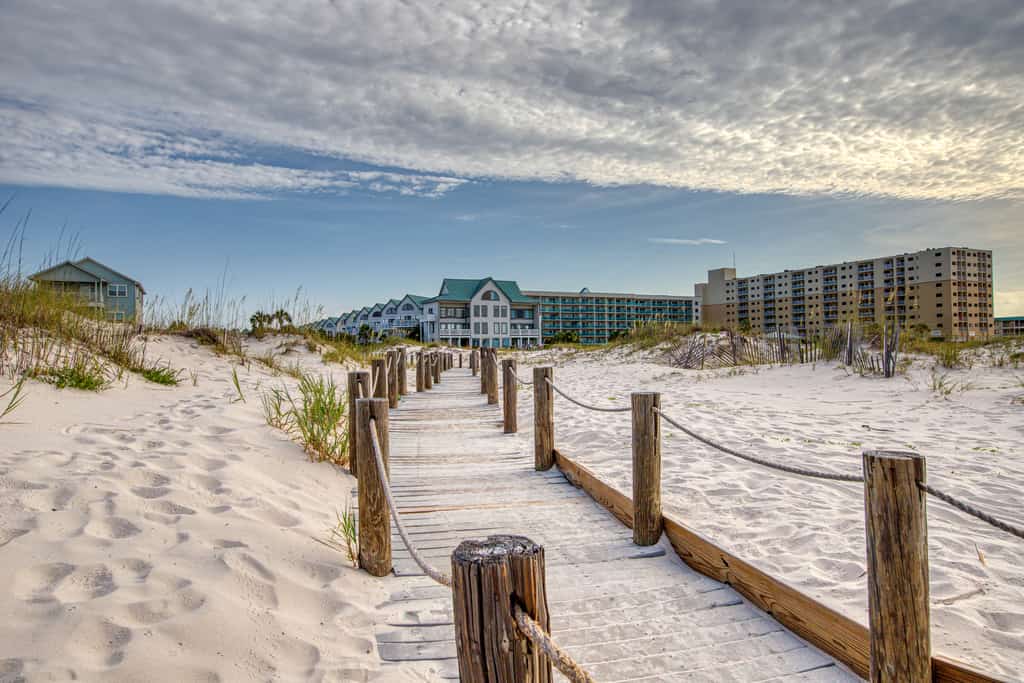 Sandy boardwalk at a beach in Gulf Shores, AL leading towards vacation condominiums.