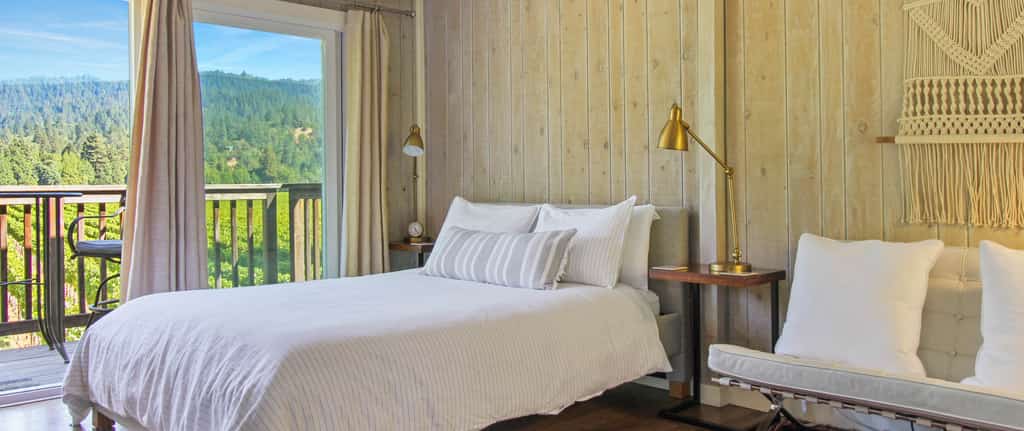 Inside a Guerneville, CA vacation rental bedroom with wooden wall panels and balcony overlooking a forest.