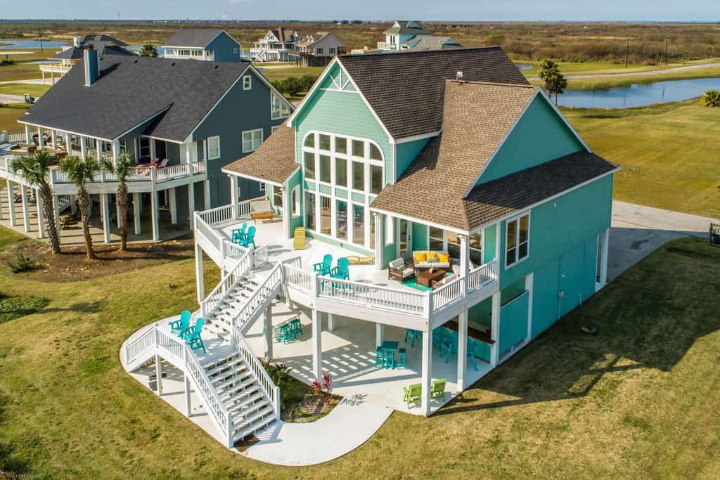 A vacation home in Port Bolivar, TX with a two level back patio with stairs near a river.