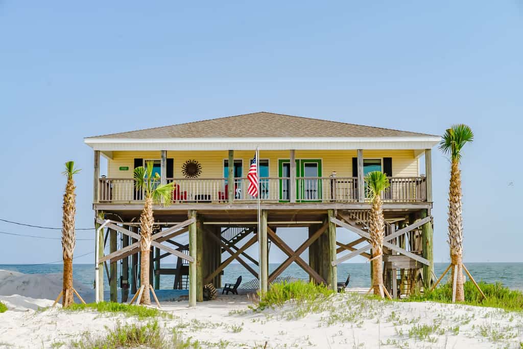pale yellow dauphin island stilt beach house framed by palm trees