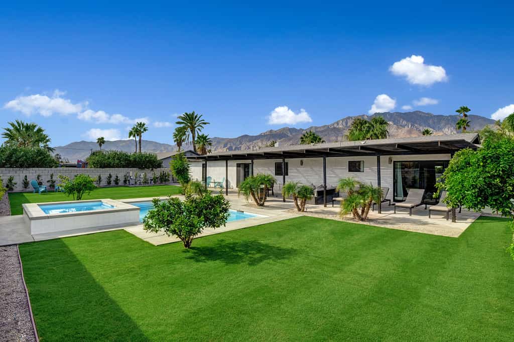 Evenly groomed back yard of a vacation rental with an outdoor pool and outdoor hot tub in Palm Springs, CA