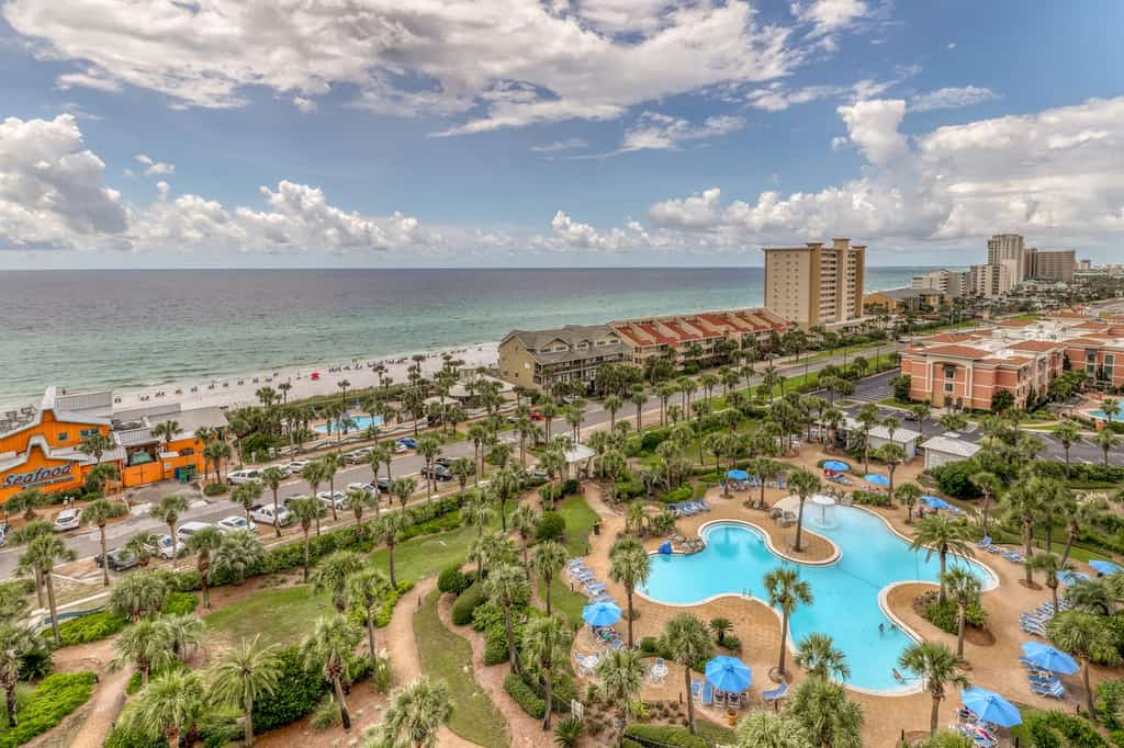 A view of Destin, FL overlooking the shore, city, main road and large outdoor pool.