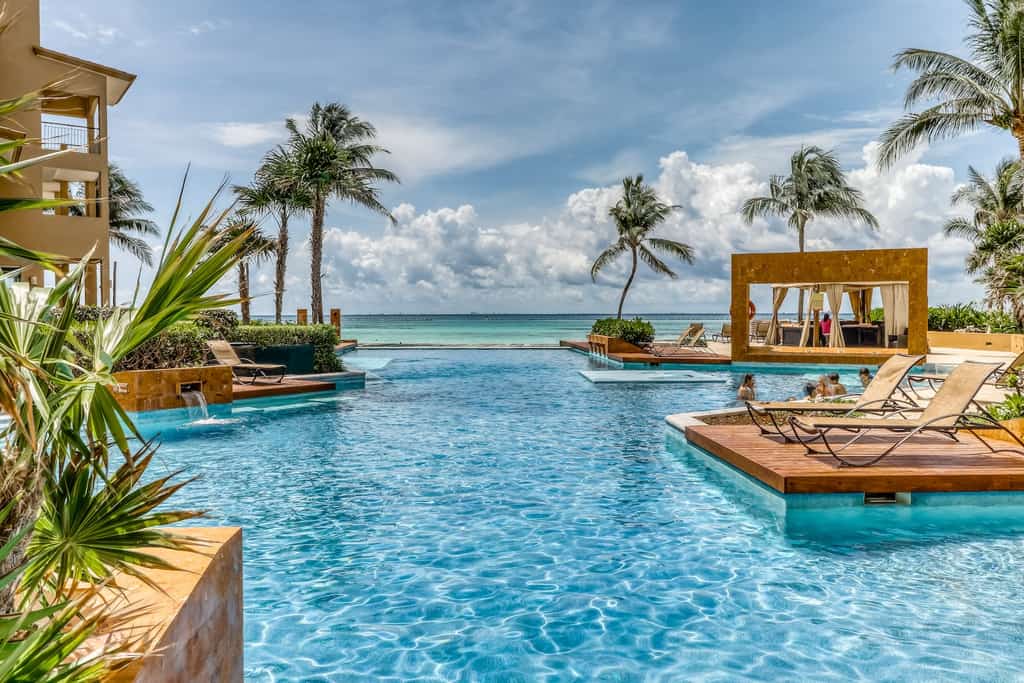 A pool overlooking the ocean with chairs and cabanas at a resort in Mexico.