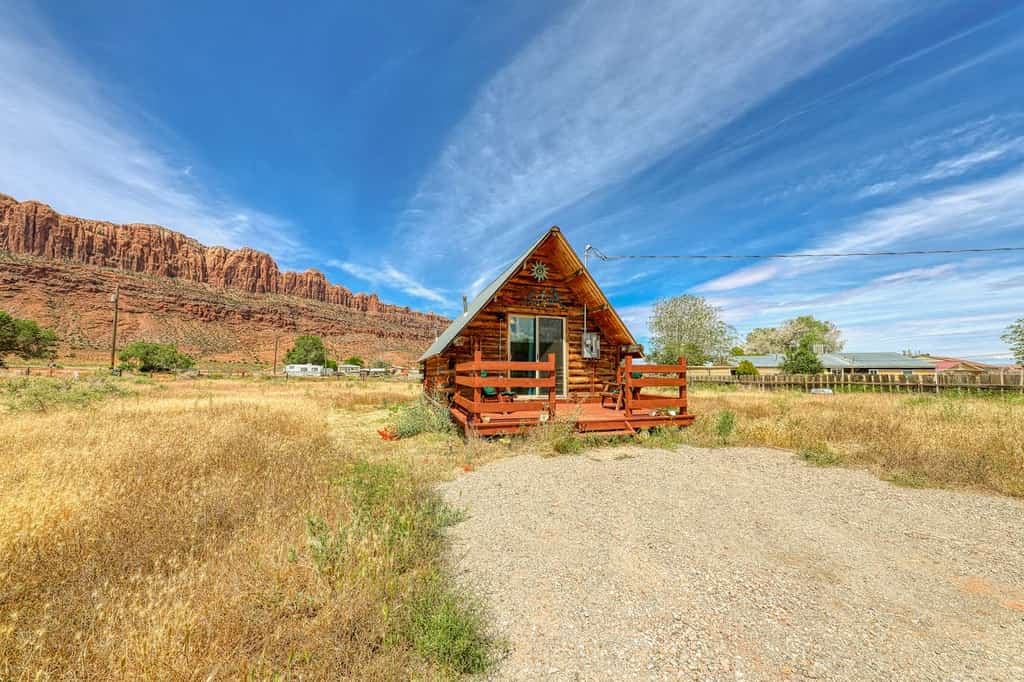 Small cabin in Utah with a gravel driveway and mountains in the back