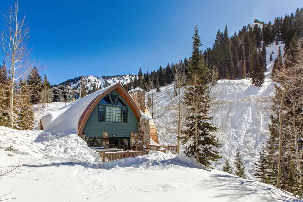A green chalet rental covered in snow on a mountain side in Alta, UT.