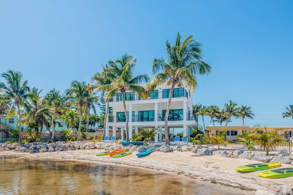 Kayaks rest on the beach near the water in front of three story beach house