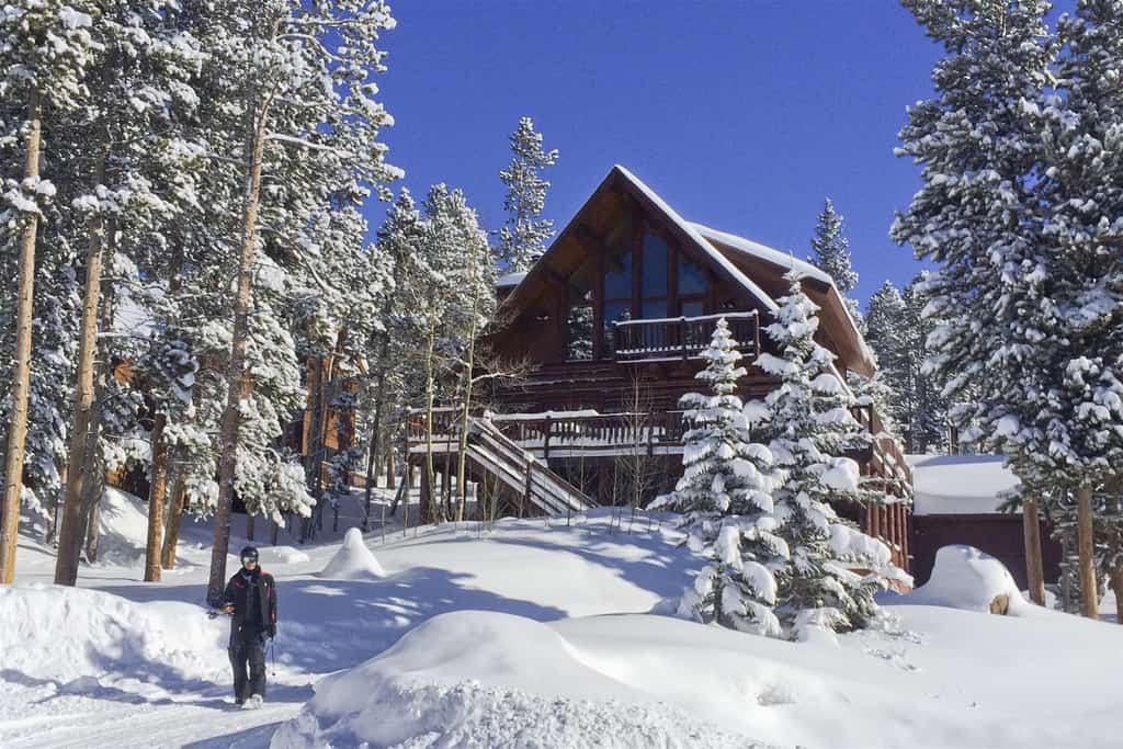 man stands in front of his breckenridge, co cabin covered in snow