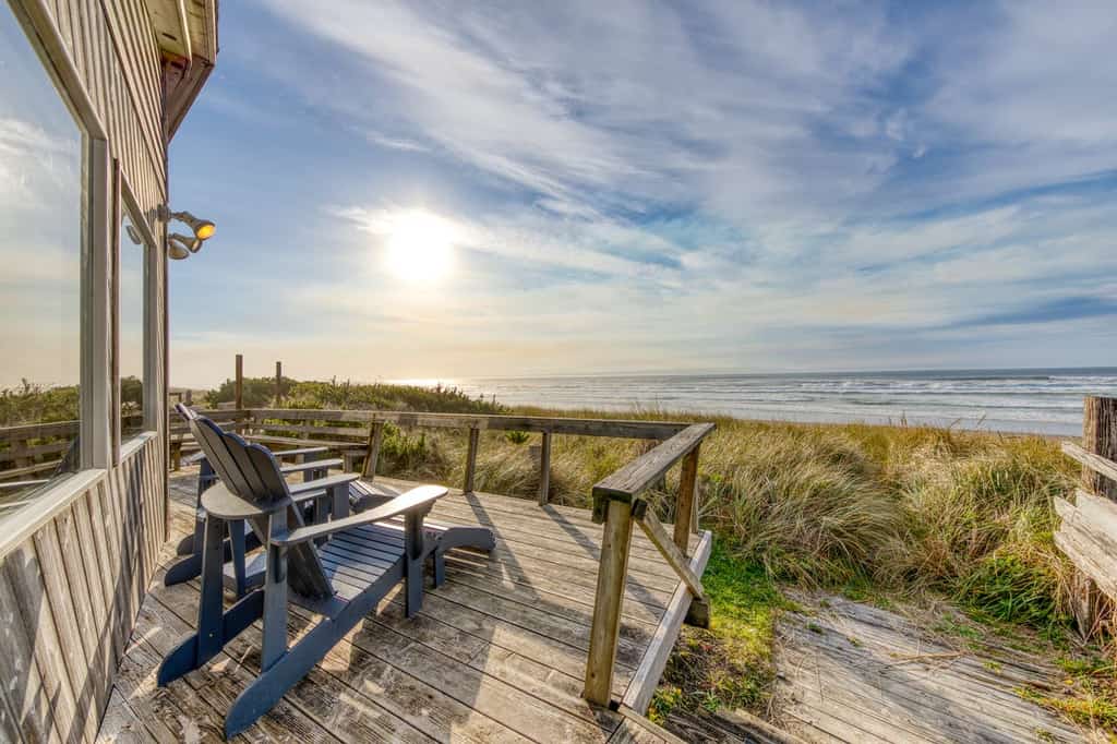 Back wooden deck of a beach rental with adirondack chairs facing the coastal shoreline in Rockaway Beach, OR.