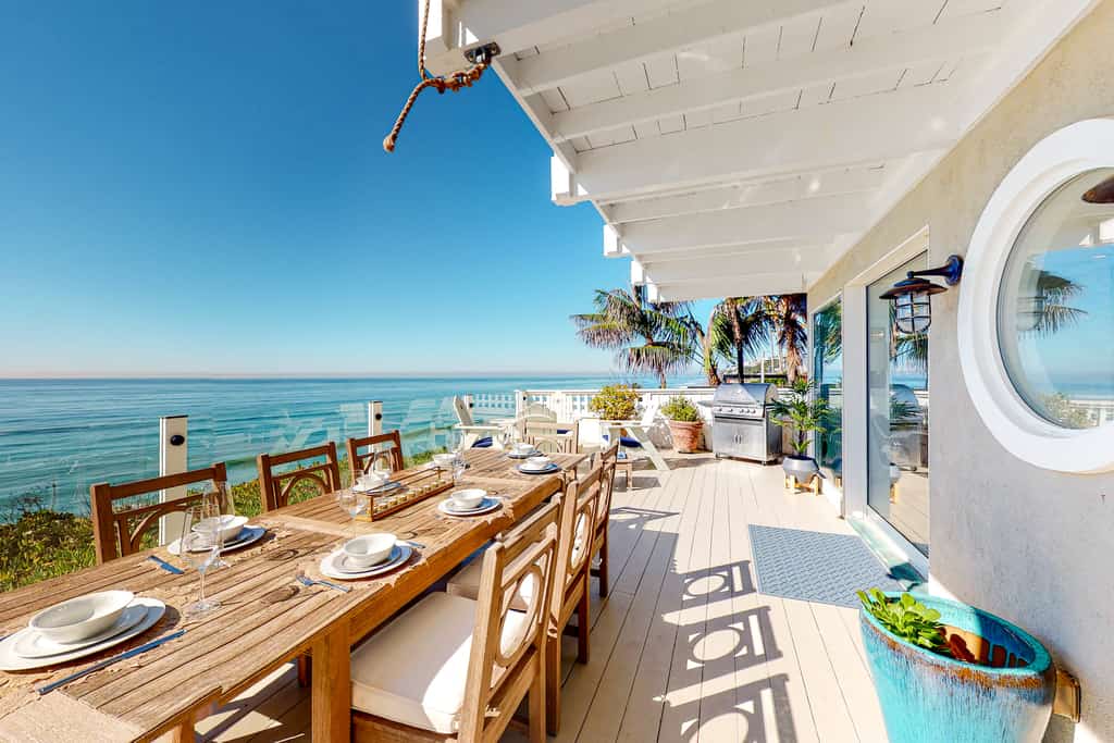 A deck with tables and chairs and other amenities overlooking the ocean at a vacation rental in Encinitas, CA.