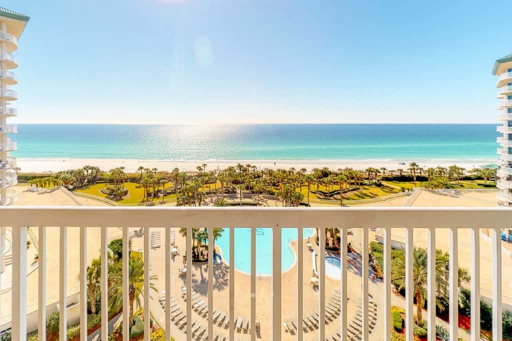 An outdoor patio at a resort in Destin, FL facing a pool and shoreline on a sunny day.