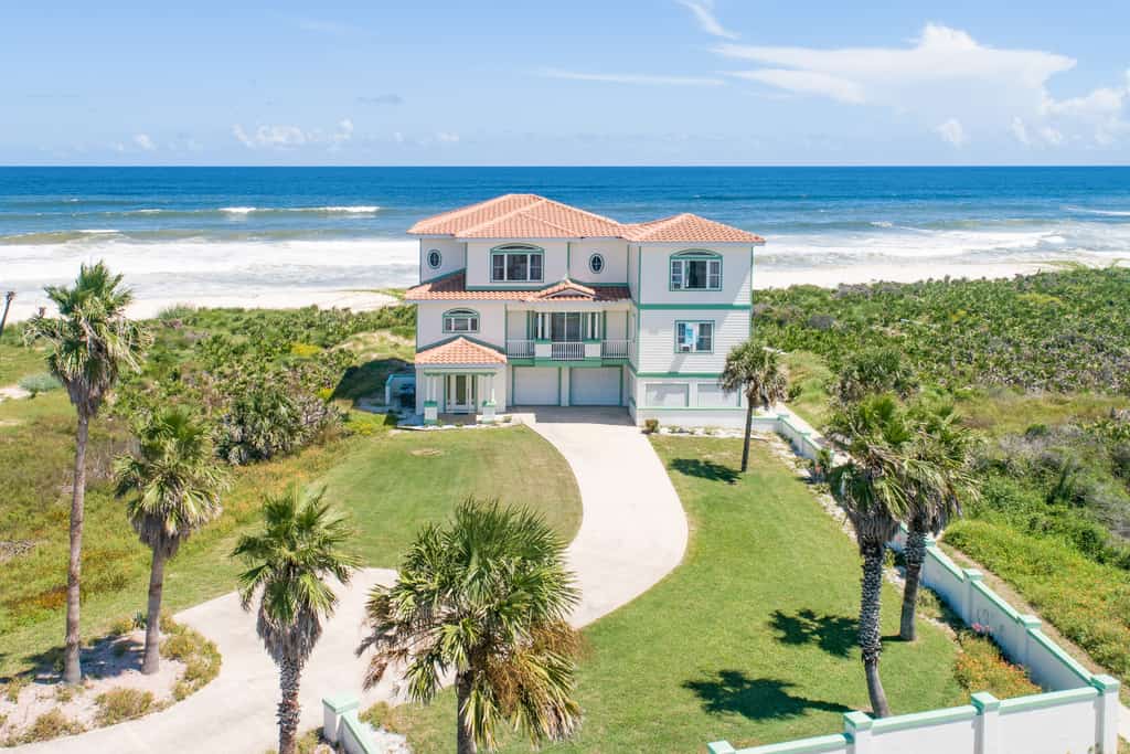 large white, oceanfront vacation home surrounded by palm trees