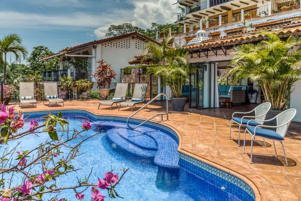 Blue outdoor pool at a vacation rental with lounger chairs and palm trees.