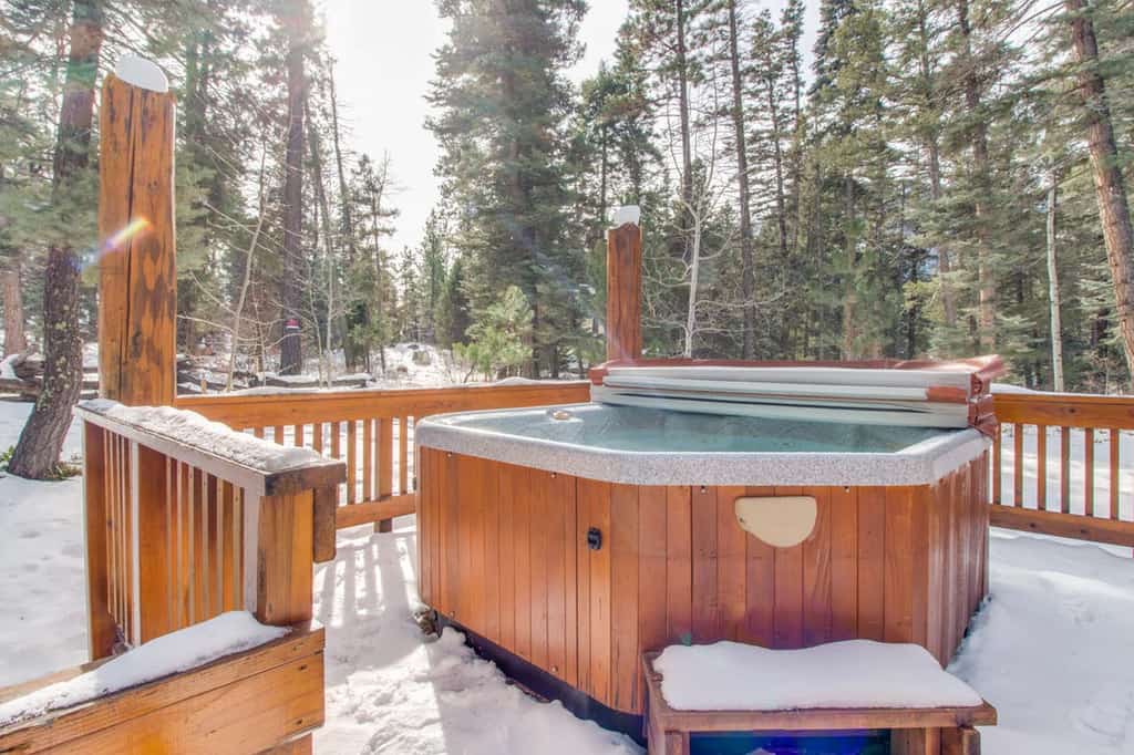 Outdoor hot tub on a wooden deck covered in snow with a view of the forest in Durango, CO