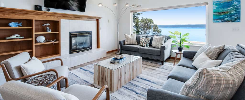 Living room of a Brinnon, WA vacation rental with a fireplace and a view of the ocean during the day.