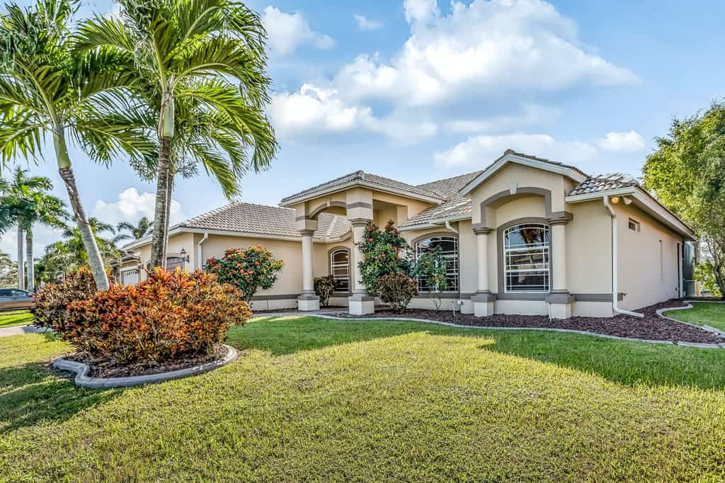 Large single family vacation rental with a yard and palm trees on a sunny day.